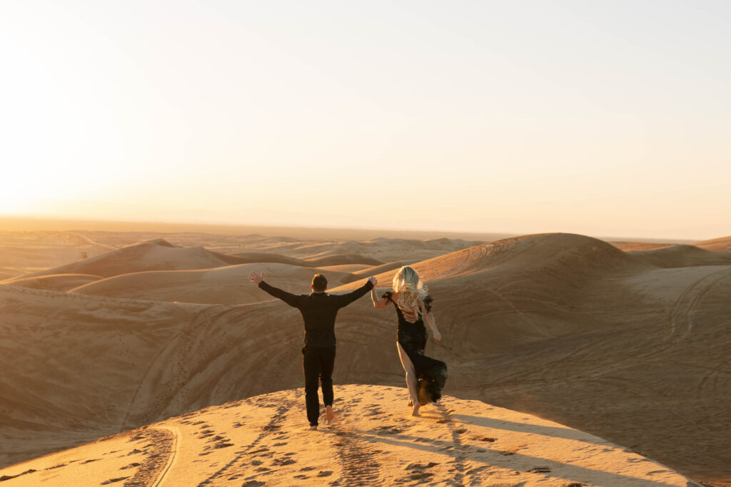 Engaged couple running through sand dunes